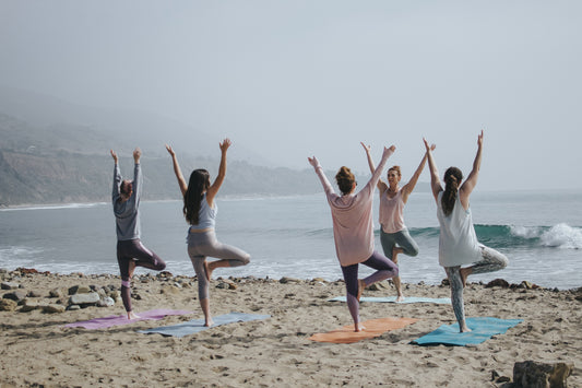 five women doing yoga on the beach