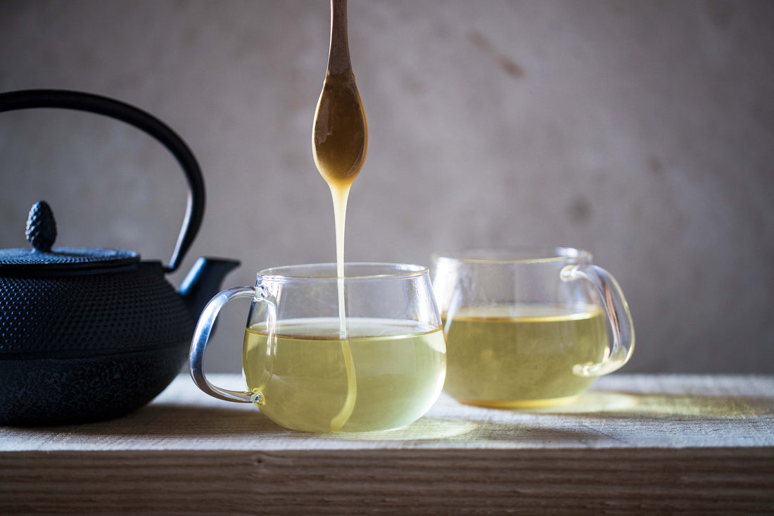 honey dripping off spoon into clear glass cup of tea
