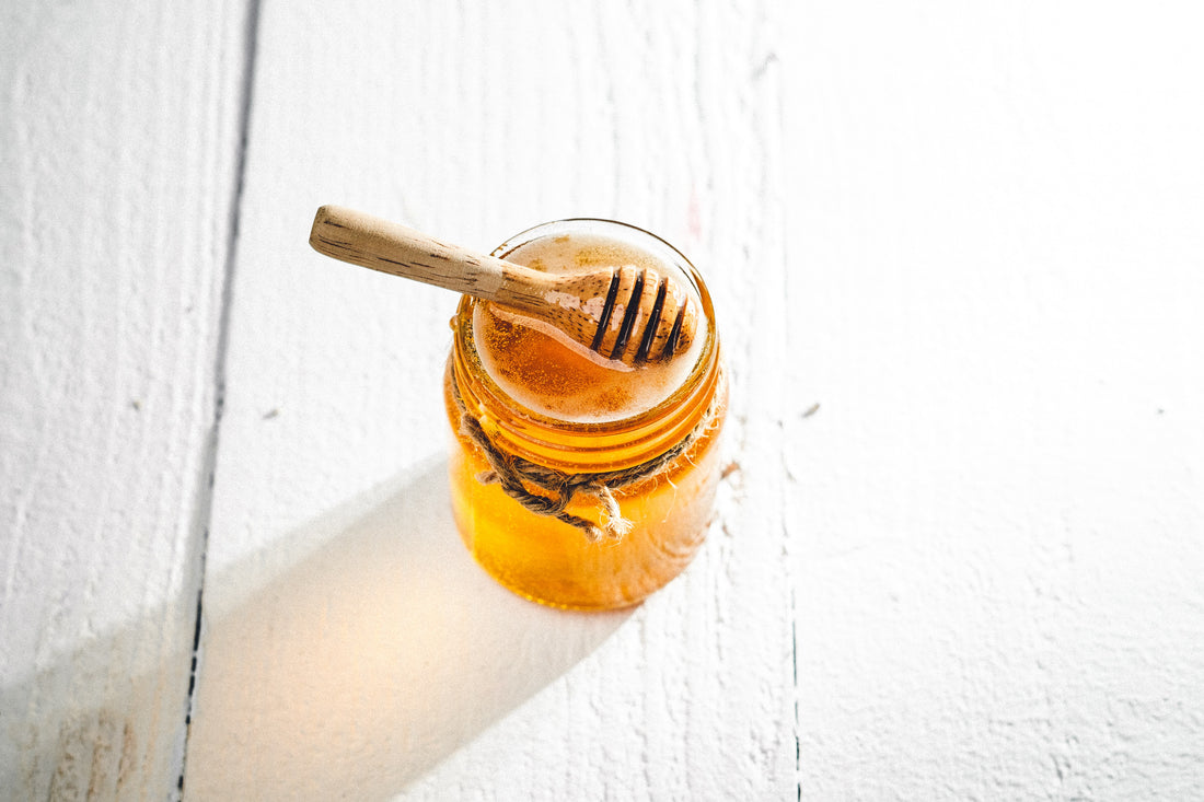 jar full of honey on white table with wood dipper