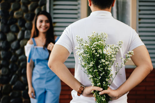 man holding flowers behind back to give to woman