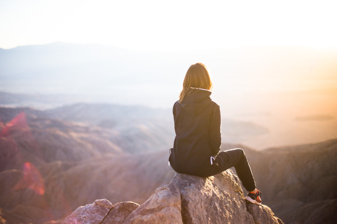 woman sitting on rock overlooking mountains during daytime